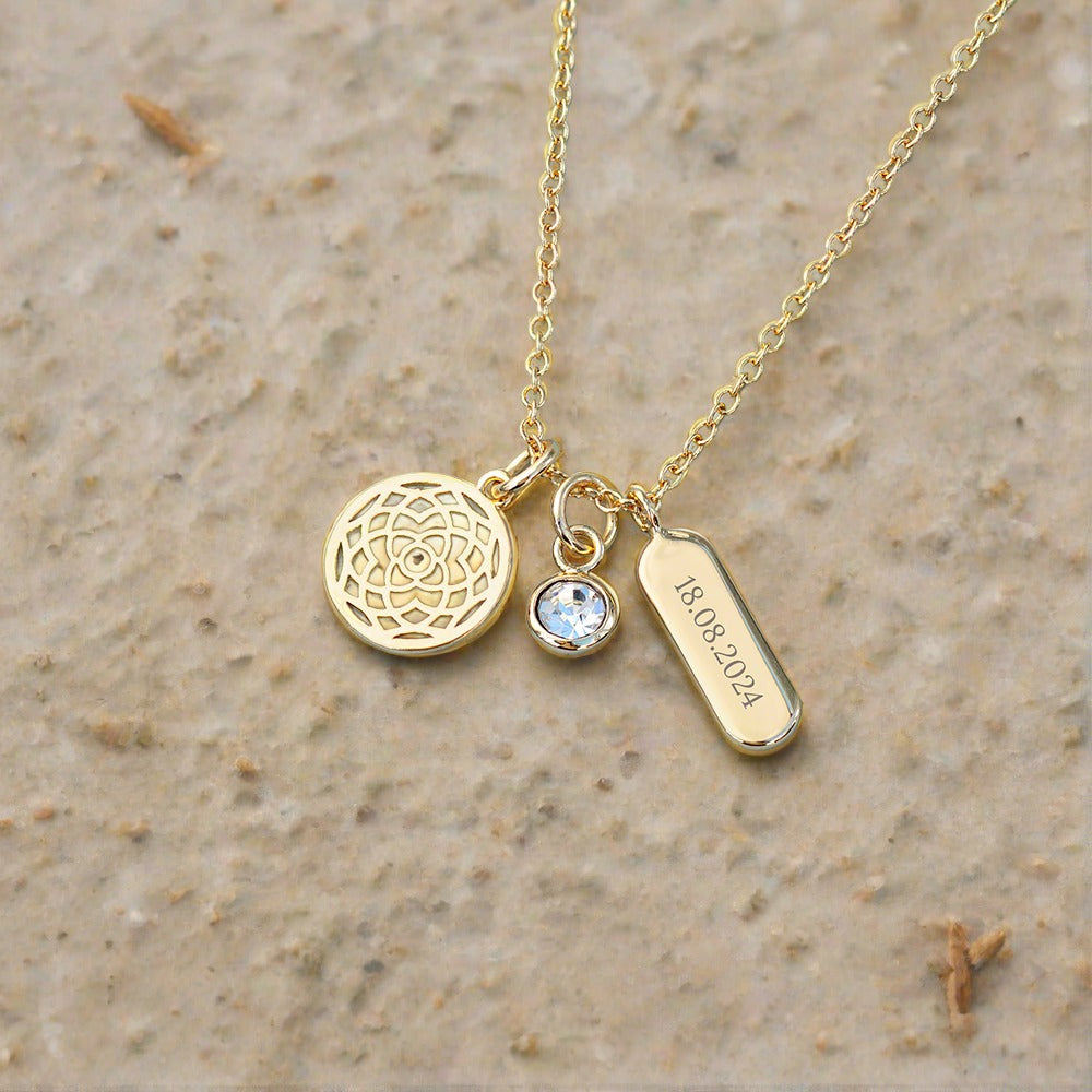 Gold coloured necklace with three charms. One manadala charm, one crystal charm and an oblong charm that can be personalised with a name or date.